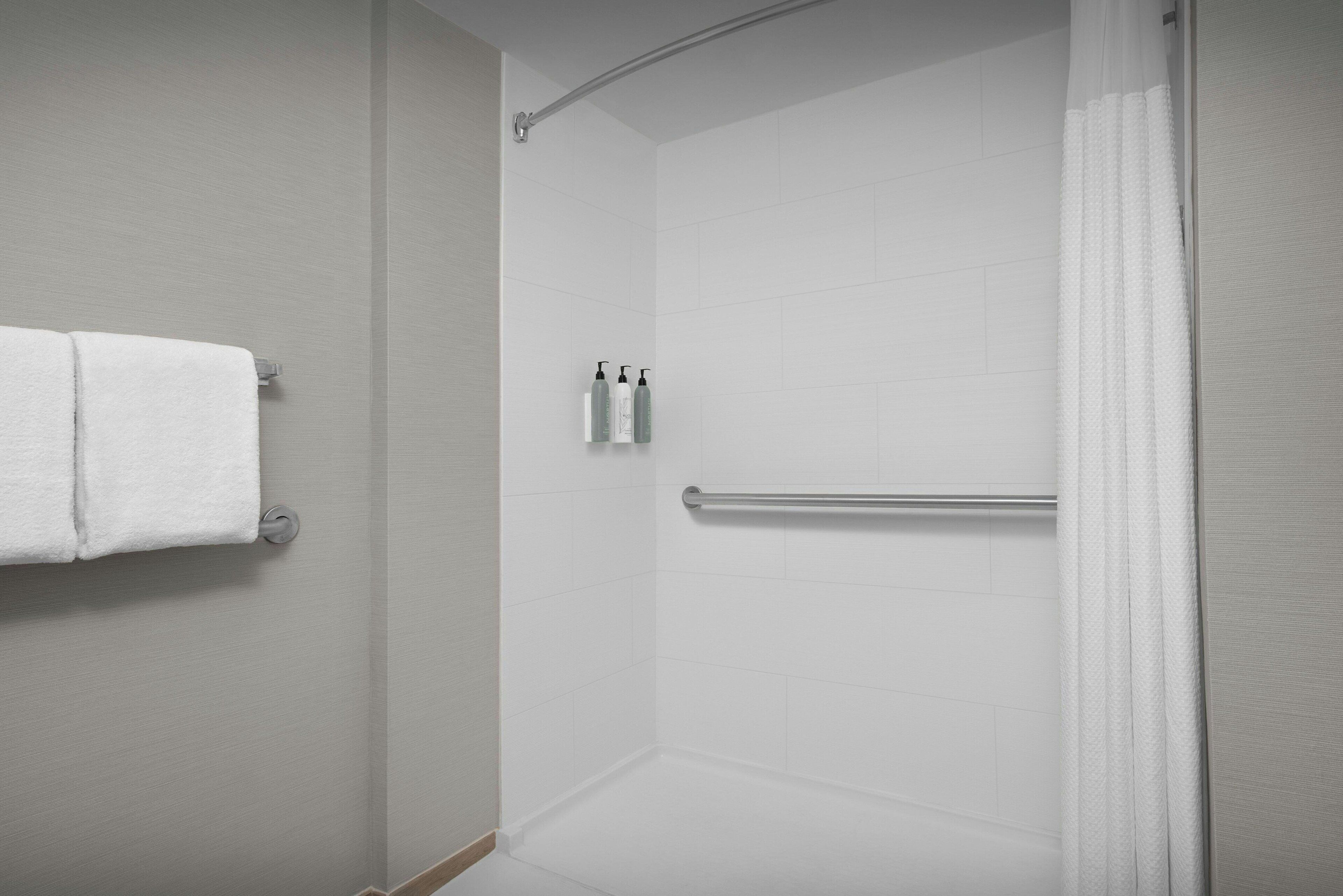Une salle de bain moderne avec des carreaux blancs, une douche avec une porte en verre, un porte-serviettes et deux bouteilles de shampoing.