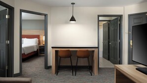 Una habitación de hotel con una cama, un escritorio con dos sillas, un televisor y un espejo.