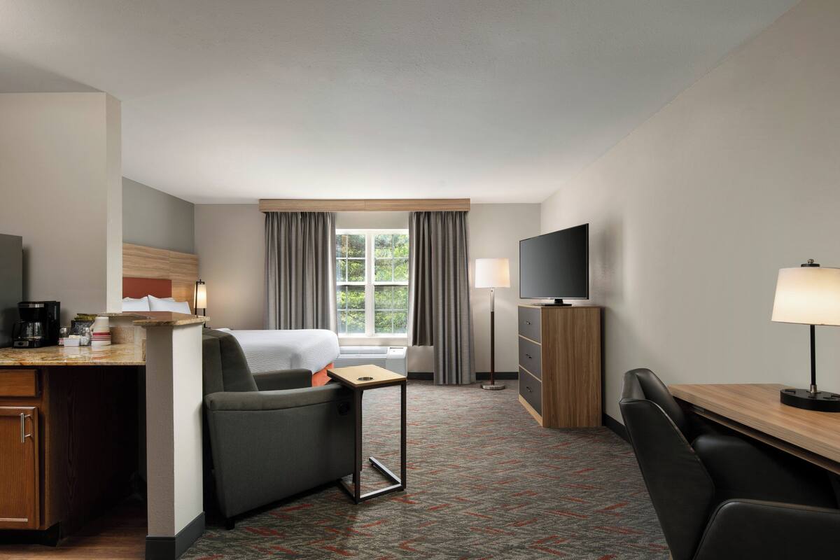 Una habitación de hotel con cama, escritorio con lámpara, televisión y ventana con cortinas.