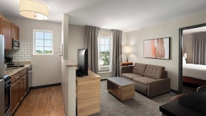 Una habitación de hotel moderna con kitchenette, un sofá, un televisor de pantalla plana y una cama.