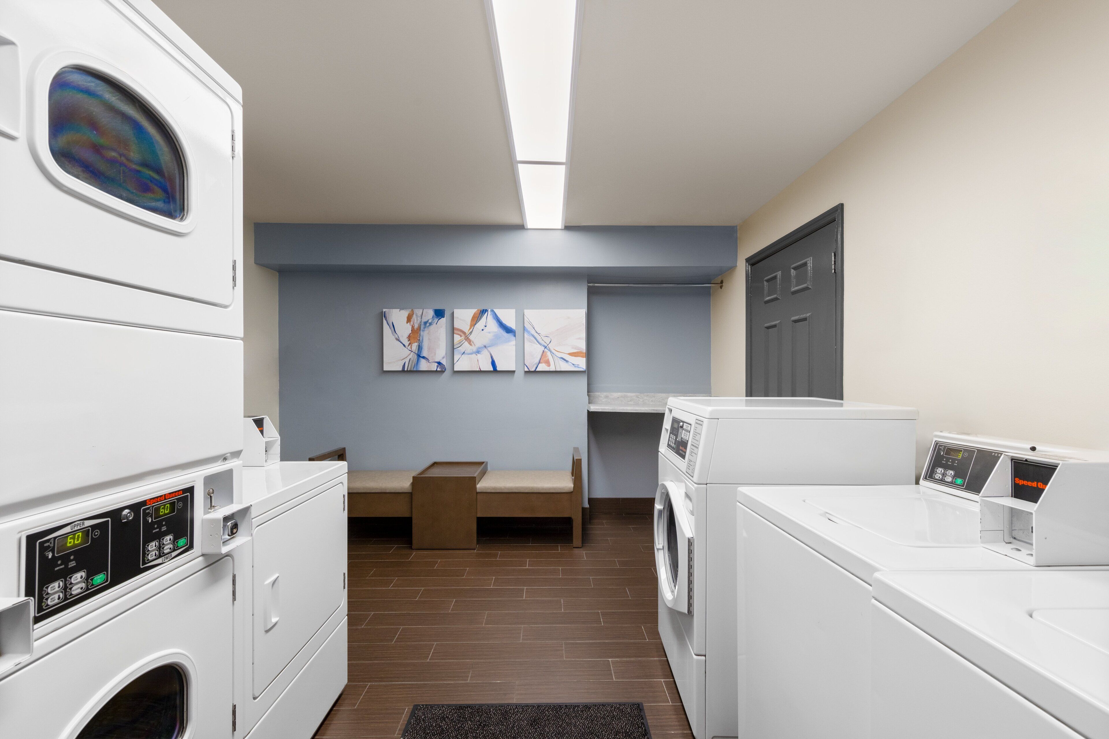 A laundry room with stacked washers and dryers, a bench, and abstract art on the wall.