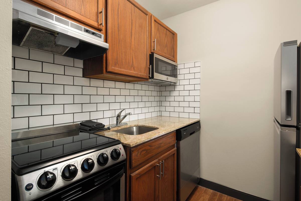 Una cocina con armarios de madera, un microondas de acero inoxidable, un lavavajillas y una estufa a gas.