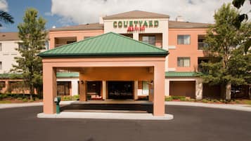 A Courtyard by Marriott hotel entrance with a green roof, a covered entrance, and a parking lot.