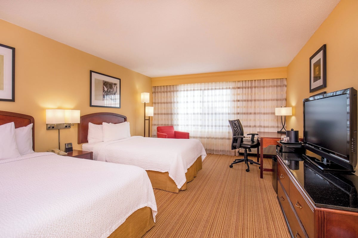 Une chambre d’hôtel avec deux lits, un bureau avec une télévision et une chaise.