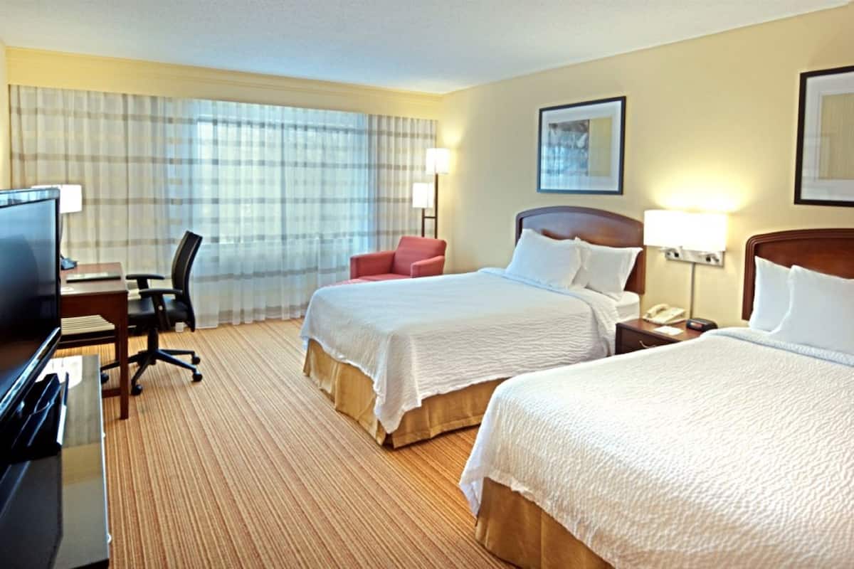 Une chambre d’hôtel avec deux lits, un bureau avec un ordinateur, une chaise, une télévision et une grande fenêtre avec des rideaux.