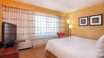 A hotel room with a bed, a television, a red chair, and two framed pictures on the wall.