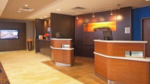 A reception area with two wooden reception desks, a digital screen, and a potted plant. - Courtyard by Marriott Hartford Manchester (Manchester)