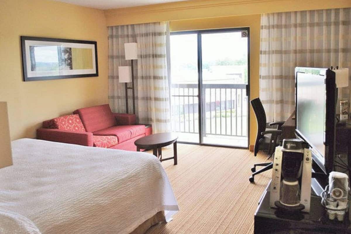 Une chambre d’hôtel avec un lit, un canapé rouge, une petite table, une télévision et une machine à café.