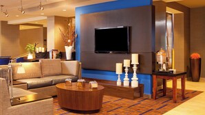 A modern hotel lobby with a sofa, a coffee table, a flat-screen TV, and a decorative vase. - Courtyard by Marriott Hartford Manchester (Manchester)
