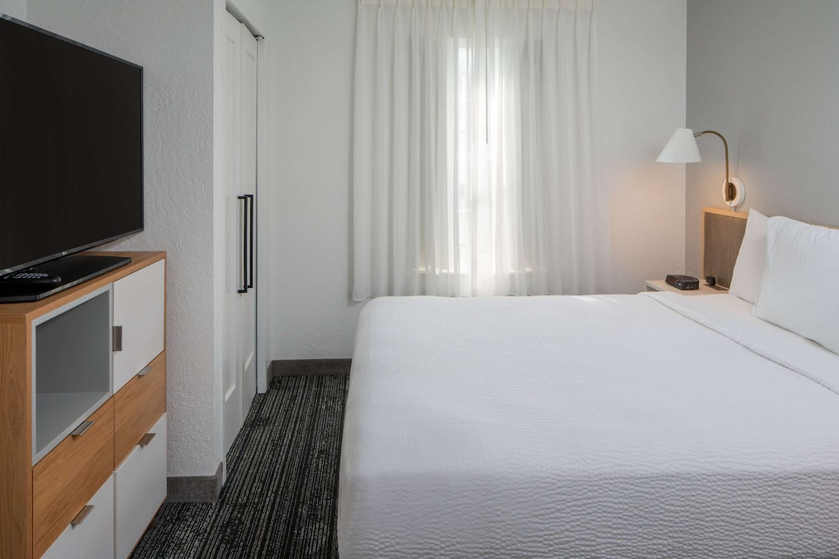 Una habitación de hotel con cama, televisión, lámpara y armario.