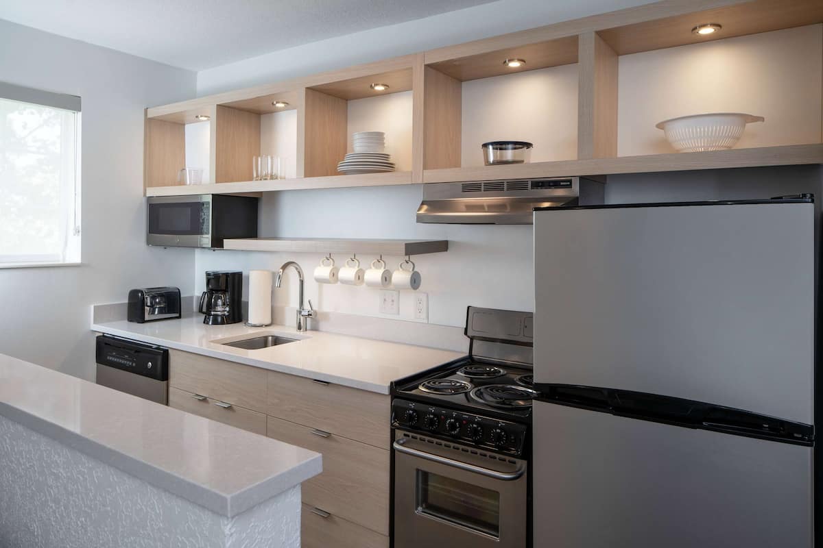 Una cocina moderna con electrodomésticos integrados, estantes de madera y encimera blanca.