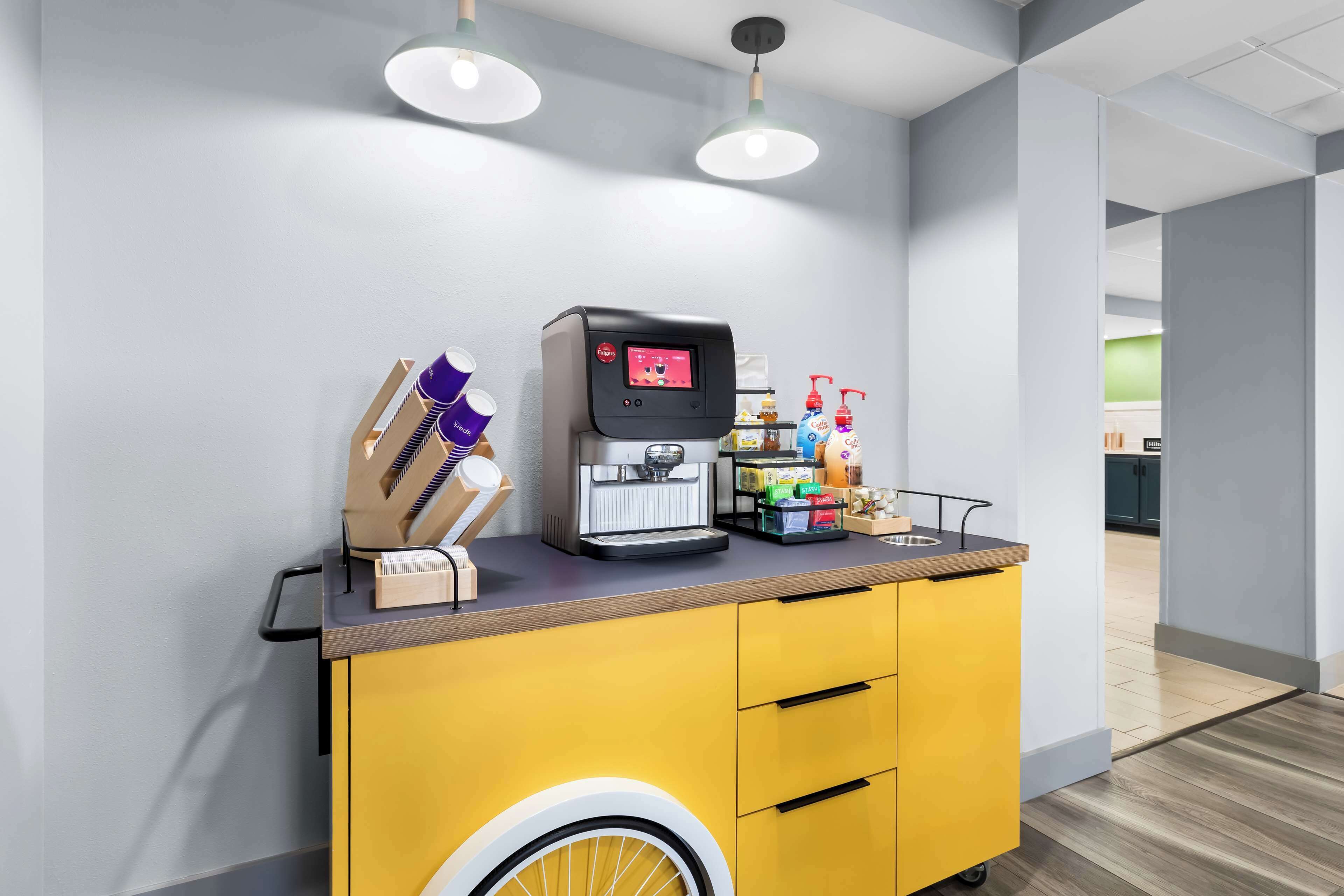 A coffee station with a coffee machine, cups, and condiments.