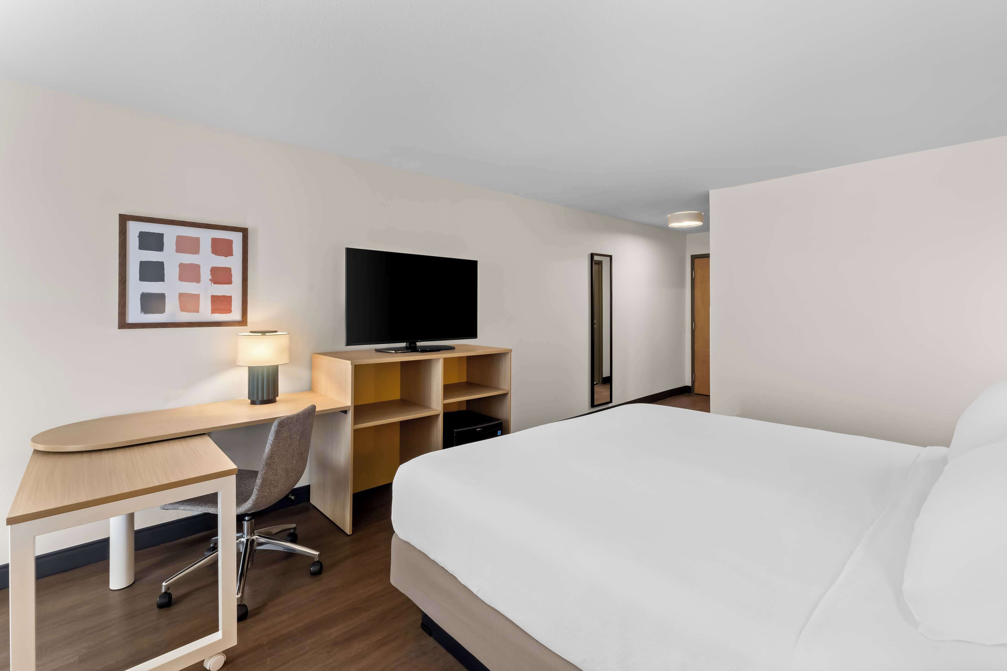 A hotel room with a bed, a desk with a chair, a television, and a lamp.