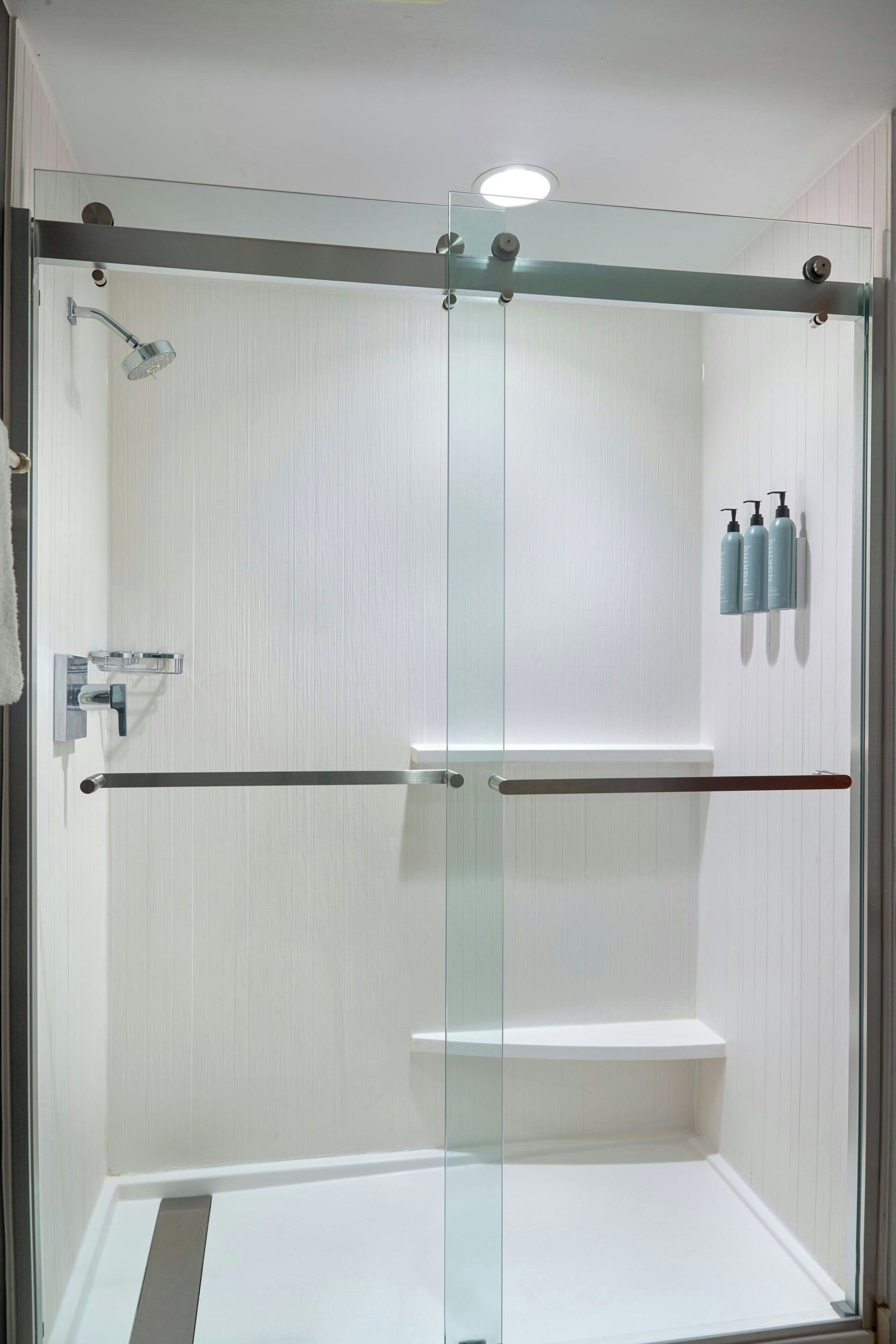 A glass-enclosed shower area with a glass door, a towel rack, and three bottles of shampoo on the wall.