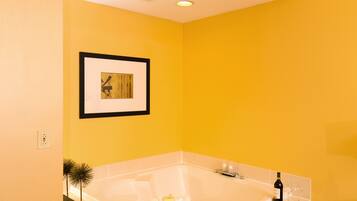 A bathroom with a large bathtub, a framed picture on the wall, and a small plant.