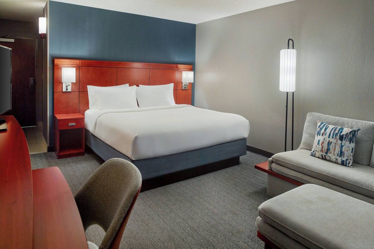 Une chambre d’hôtel comprenant un lit, un bureau, une chaise, un canapé et une lampe sur pied.