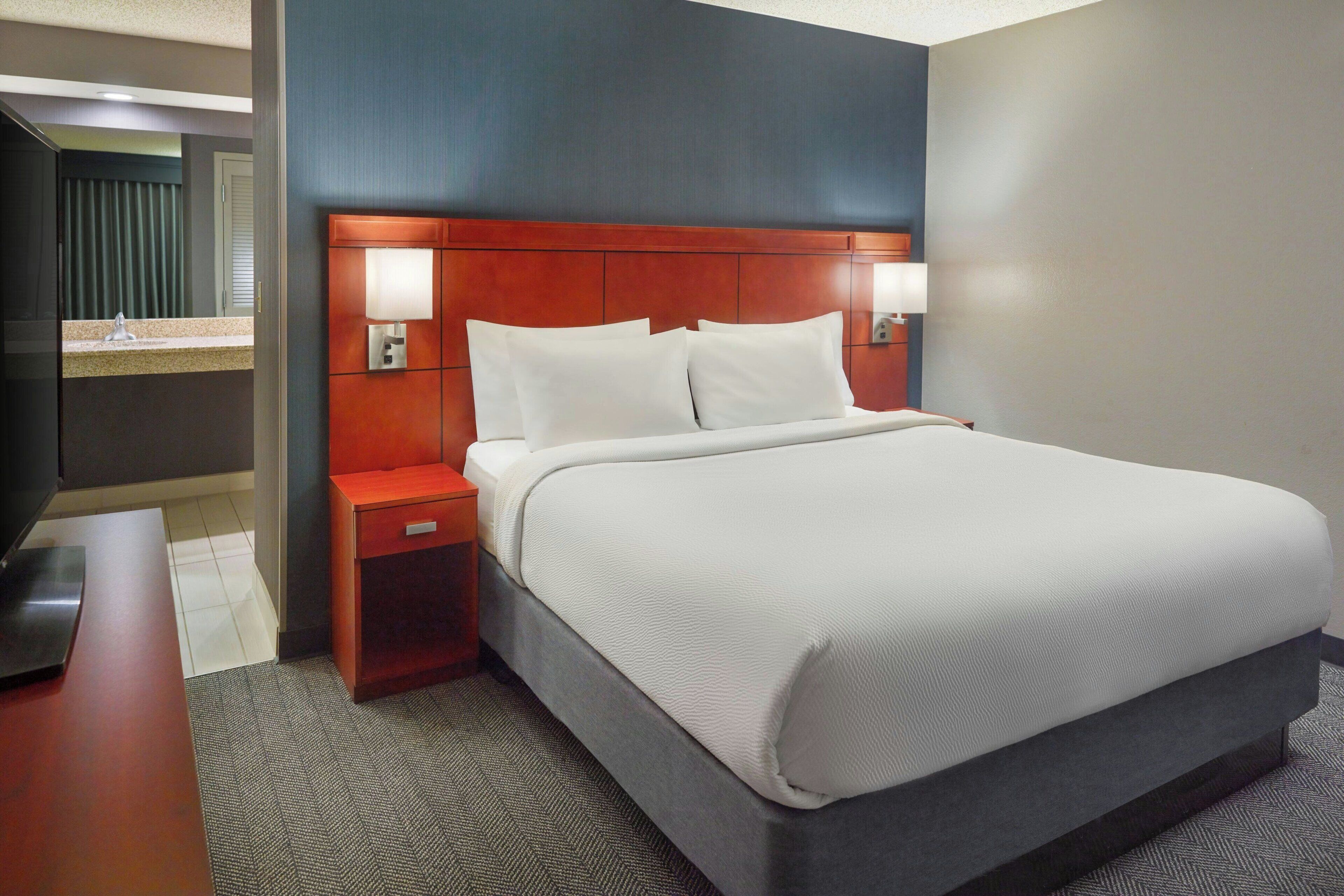 A hotel room with a large bed, a wooden headboard, two bedside lamps, a nightstand, and a television.