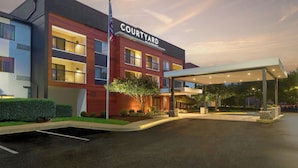 Ein Courtyard by Marriott Hotel mit überdachter Eingangspforte, einer Fahnenstange und einer begrünten Anlage.