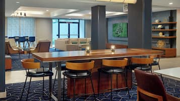 Un moderno vestíbulo de hotel con zona de bar, asientos y una gran pantalla mostrando un partido de fútbol.