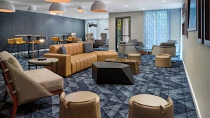 Eine moderne Hotelhalle mit einem geometrischen Teppichmuster, Ledersitzmöbeln und Pendelleuchten.
