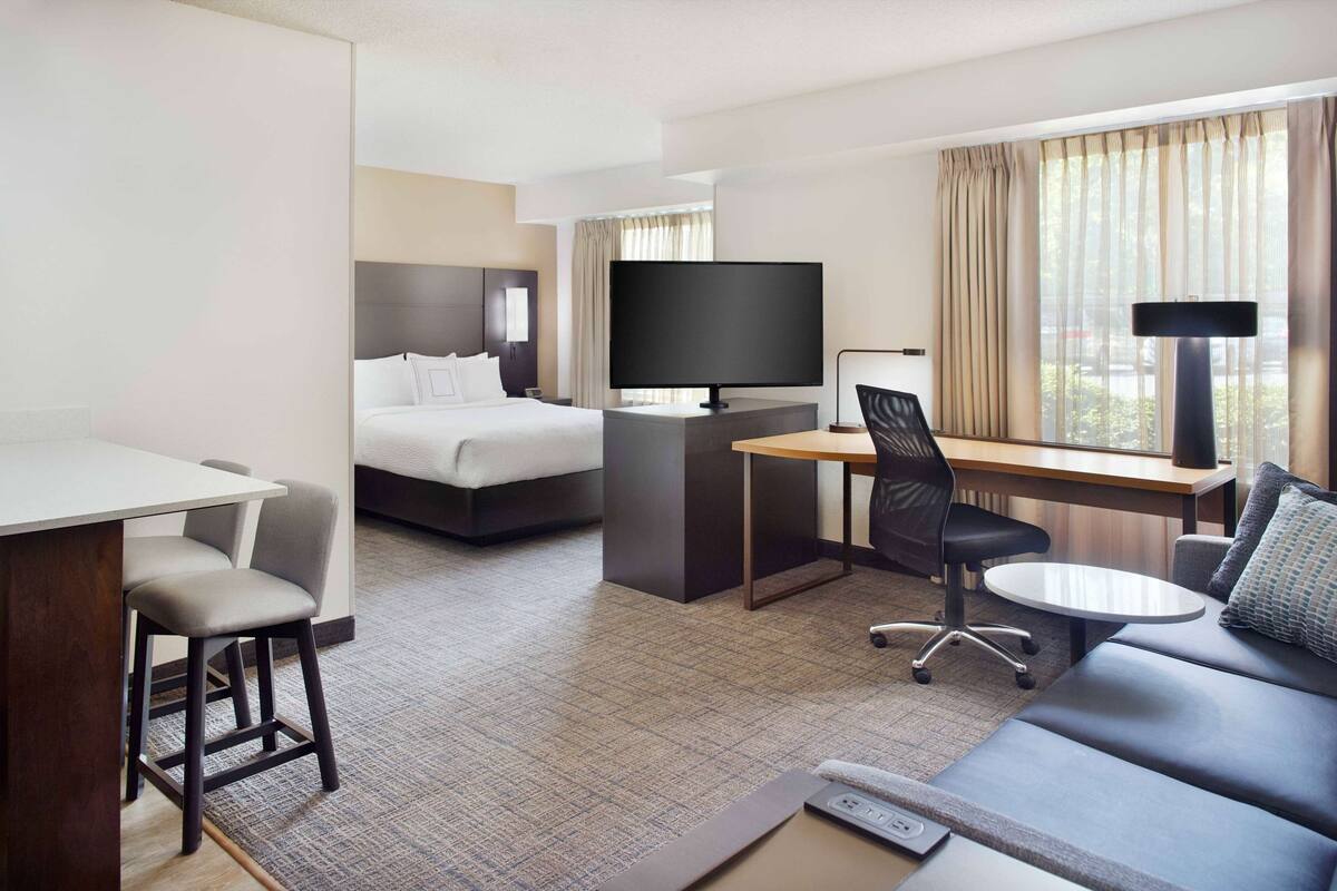 A hotel room with a bed, a desk with a TV, a sofa, and a chair.