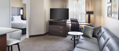 A hotel room with a bed, a desk with a television, a sofa, and a small table.