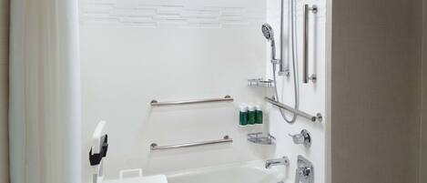 A modern bathroom with a bathtub, shower, and handrails.