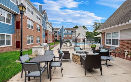 A patio area with outdoor seating, a fire pit, and a pool in the background.