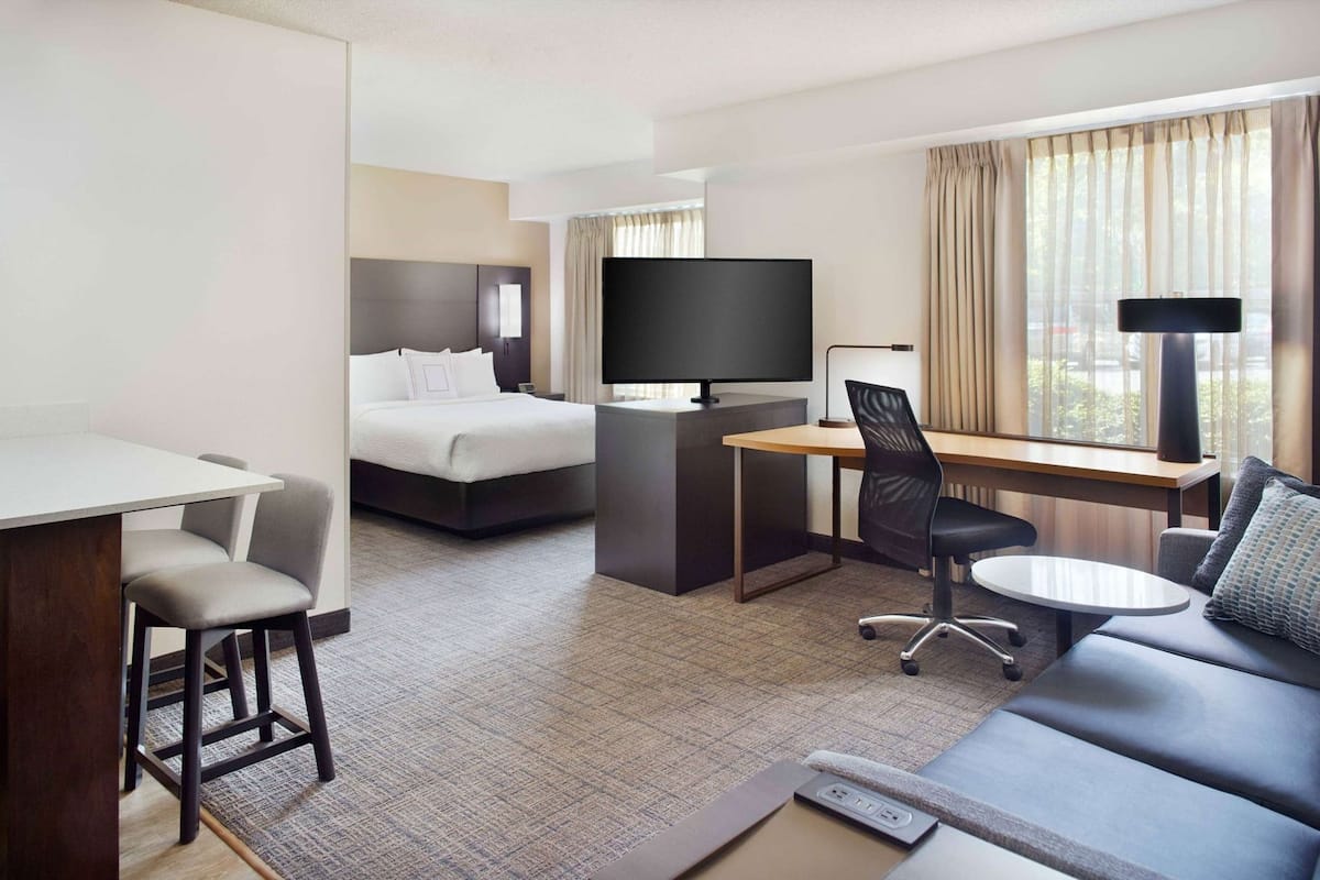 A hotel room with a bed, desk, TV, and seating area.
