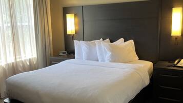 Habitación de hotel con una cama grande, dos mesitas de noche, un cabecero y dos lámparas fijadas a la pared.