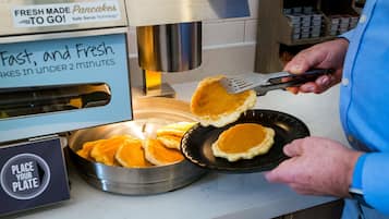 A person cooking pancakes on a griddle with a spatula.