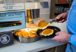 A person cooking pancakes on a griddle with a spatula.