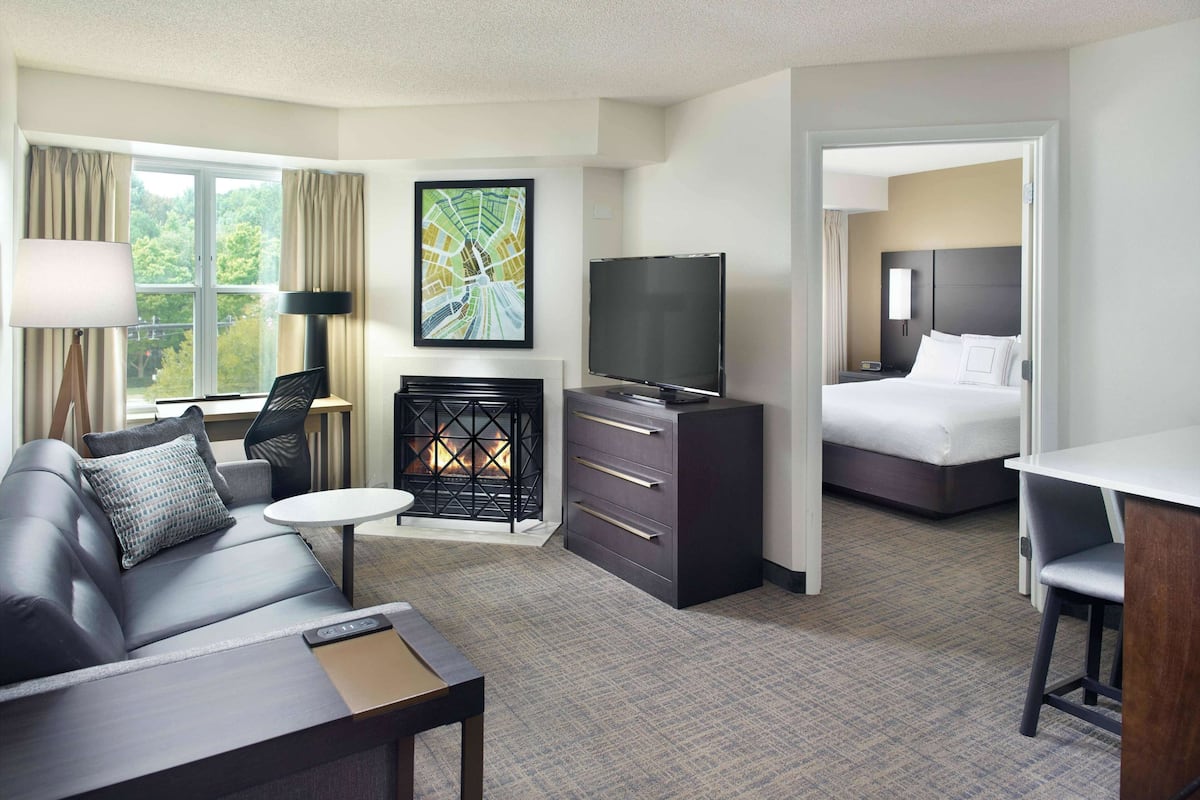 A hotel room with a sofa, a TV, a fireplace, a bed, and a desk.