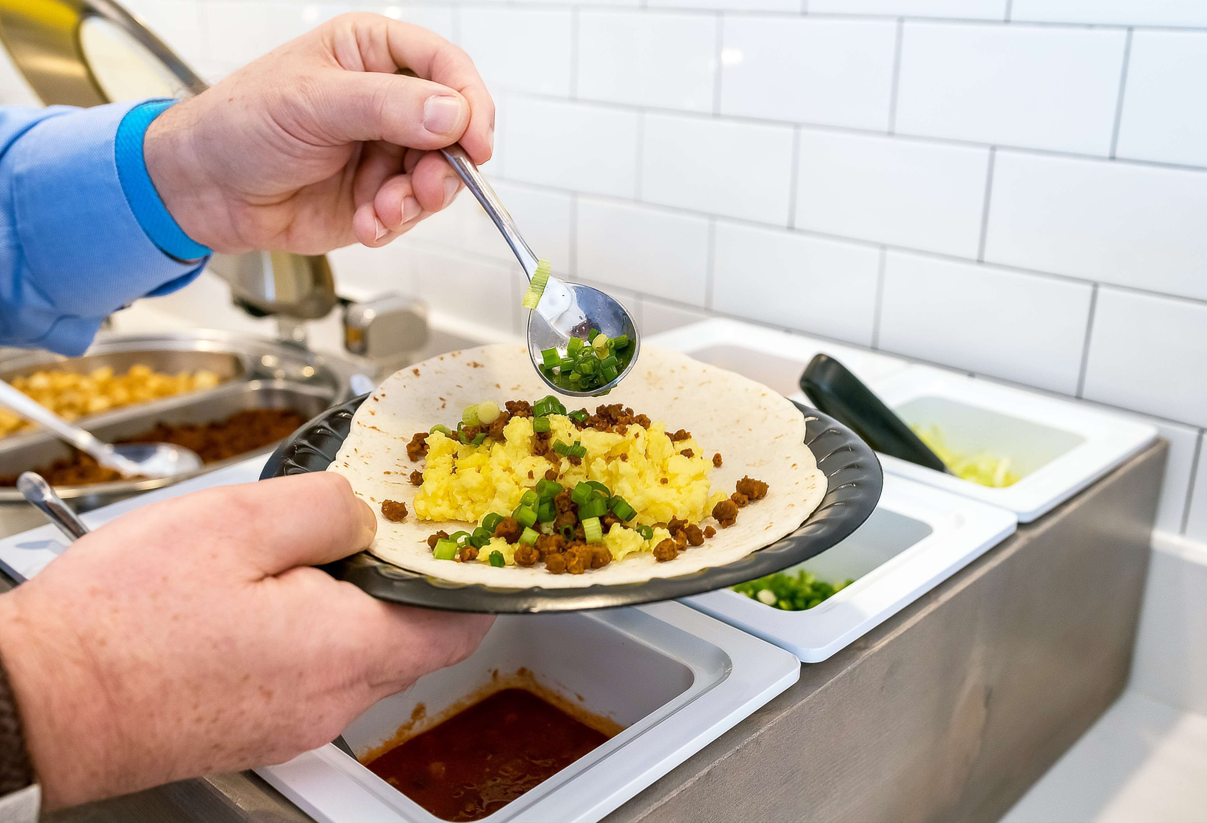 A person holding a plate with a food item topped with green onions.