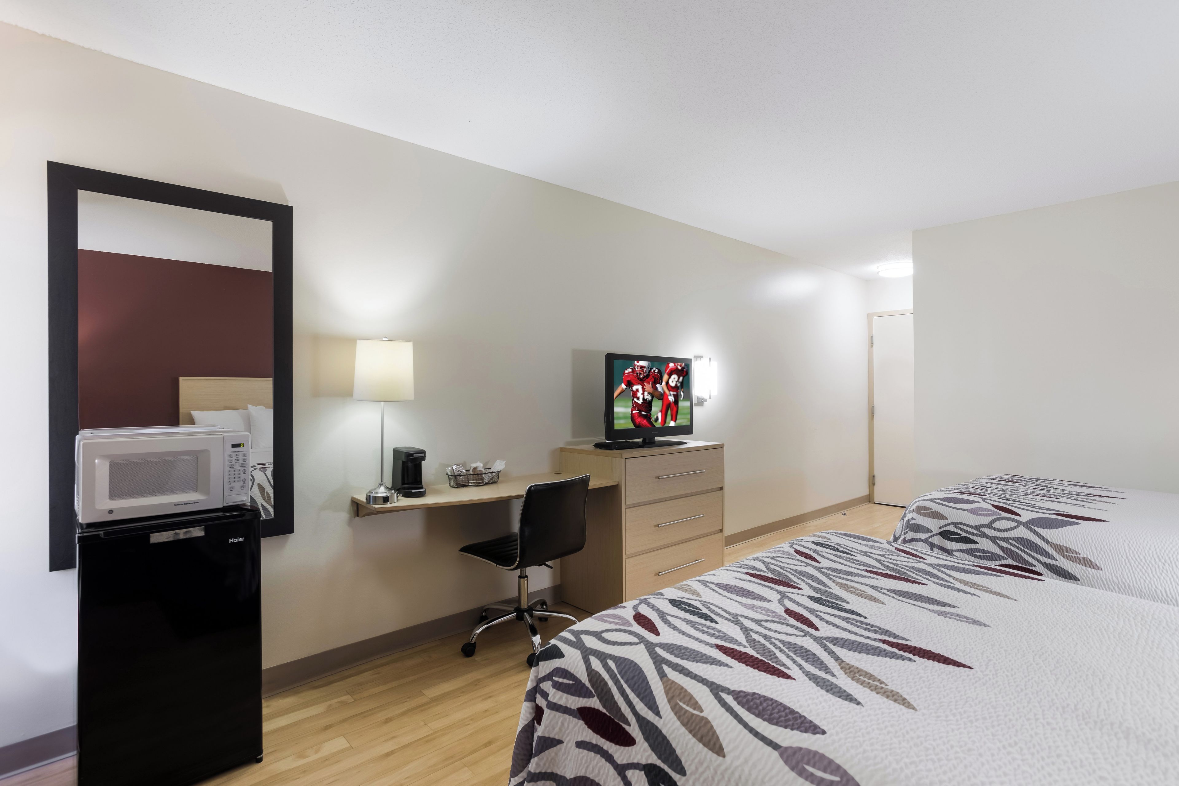 Ein Hotelzimmer mit Bett, Schreibtisch, Fernseher, Mikrowelle und einem Sessel.