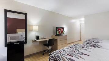 Ein Hotelzimmer mit Bett, Schreibtisch, Fernseher, Mikrowelle und einem Sessel.