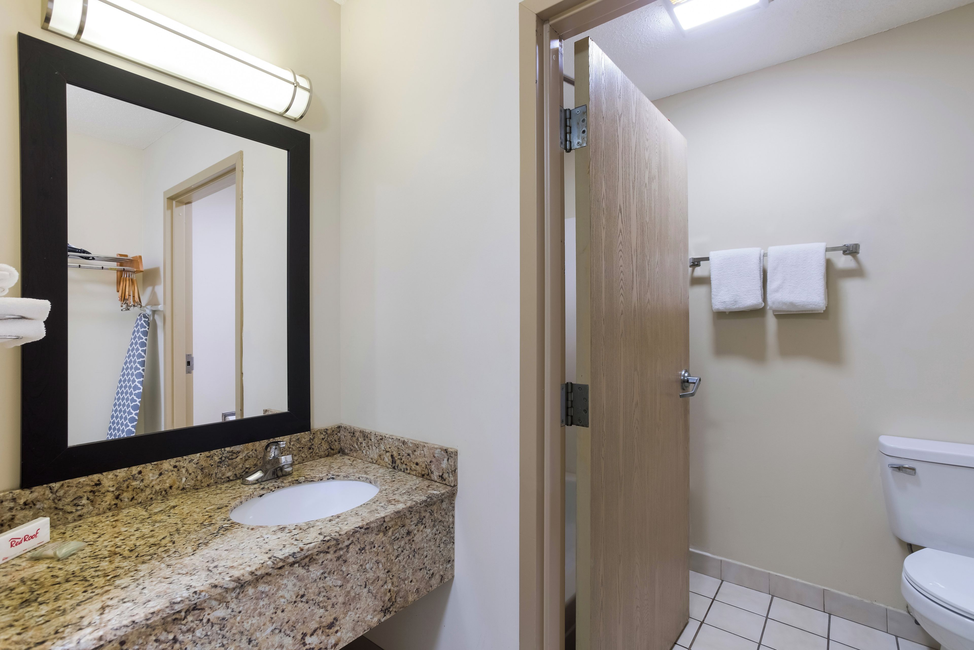 A bathroom with a granite countertop sink, a mirror with a black frame, a towel rack with towels, and a toilet.