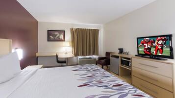 Habitación de hotel con cama, escritorio, televisor, silla y lámpara de escritorio.