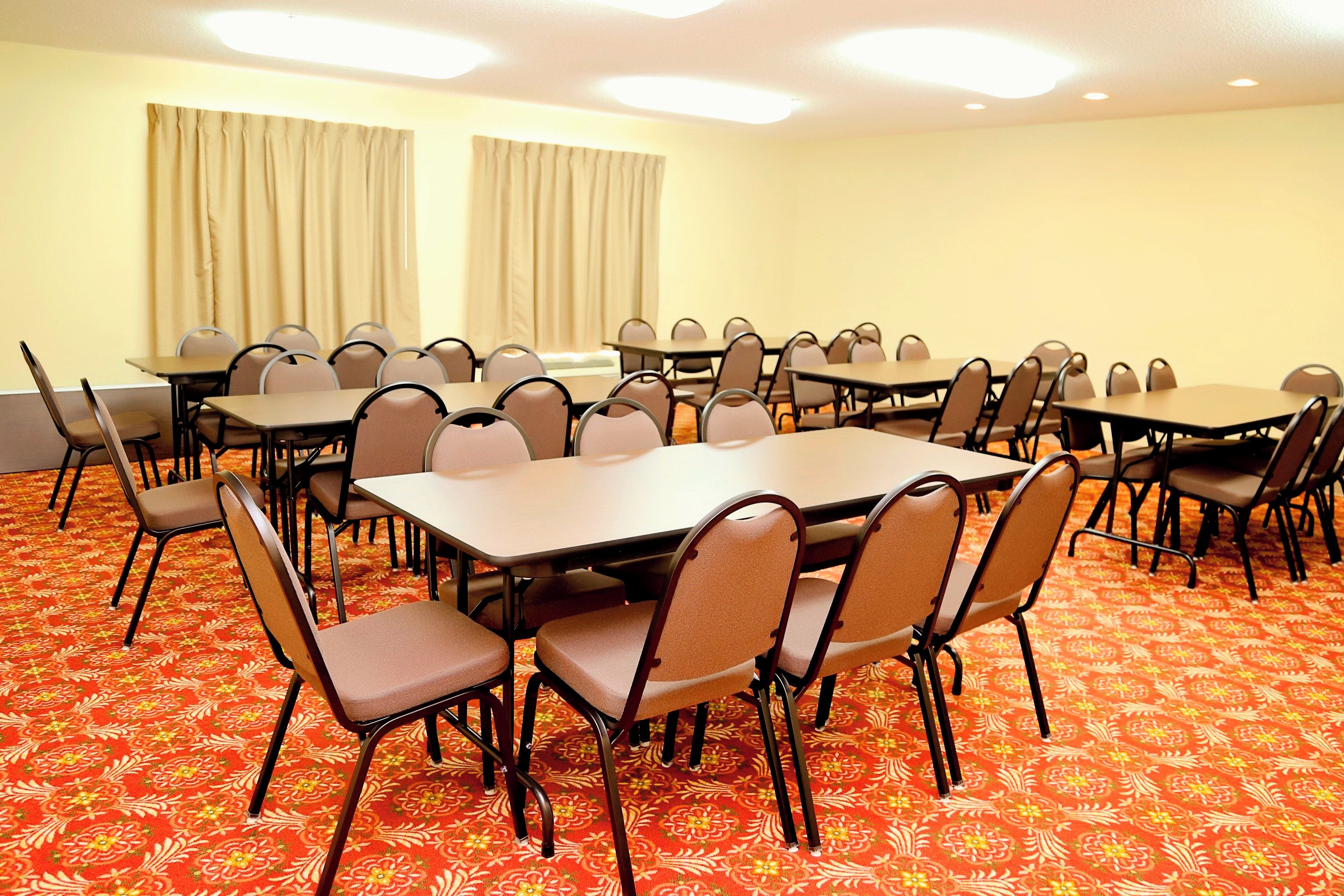 A conference room with multiple tables and chairs, carpeted floor, and curtains on the windows.
