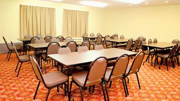 A conference room with multiple tables and chairs, carpeted floor, and curtains on the windows.