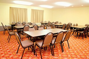 Un salón de conferencias con varias mesas y sillas, piso alfombrado y cortinas en las ventanas.