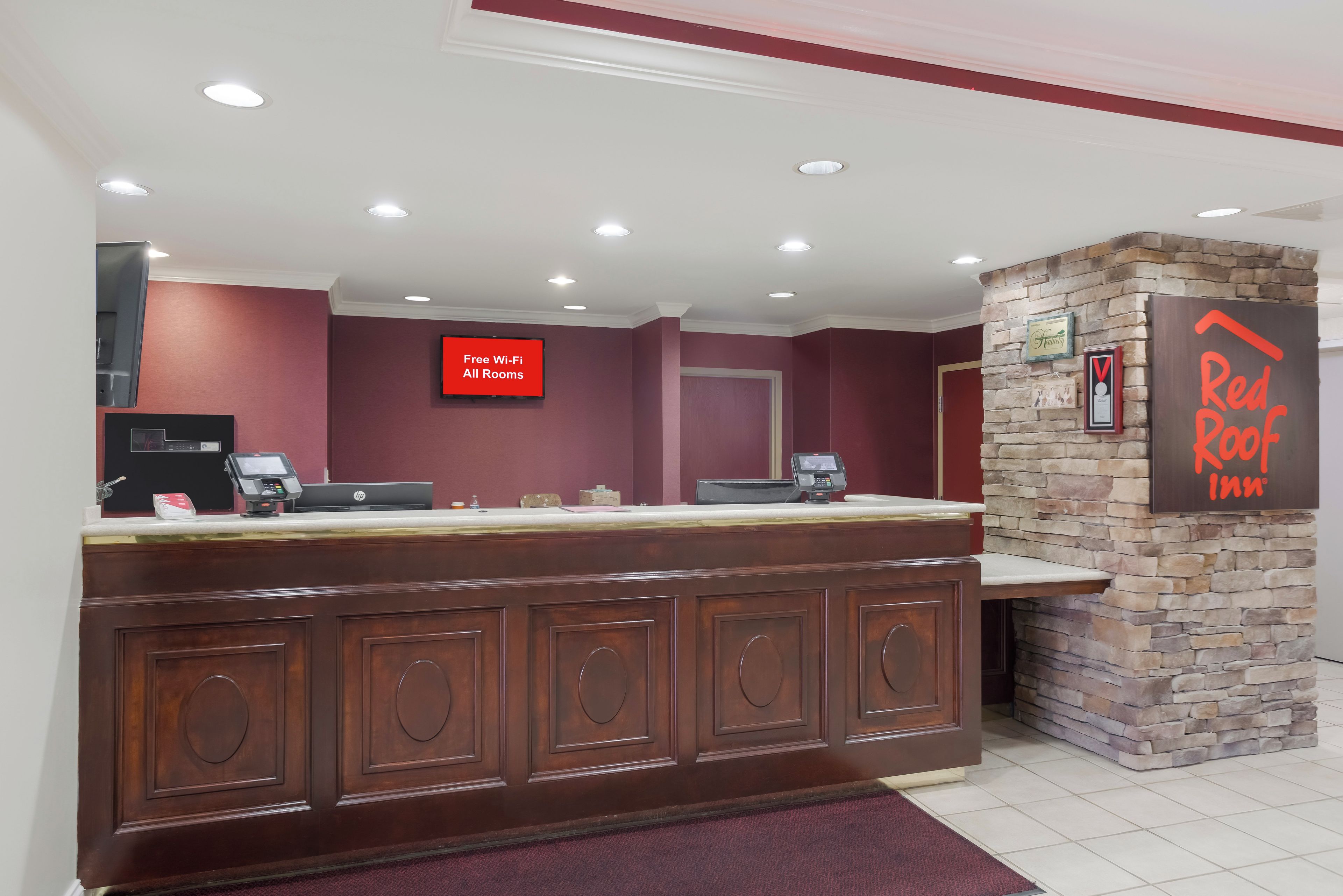 A reception desk with a sign indicating free Wi-Fi in all rooms, a Red Roof Inn sign, and a stone wall.