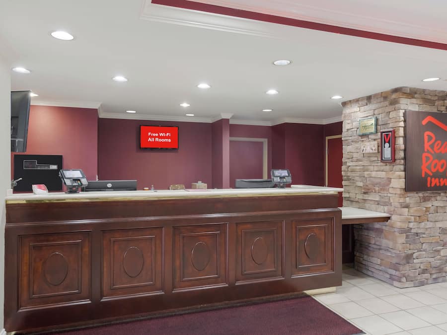 A reception desk with a sign indicating free Wi-Fi in all rooms, a Red Roof Inn sign, and a stone wall.