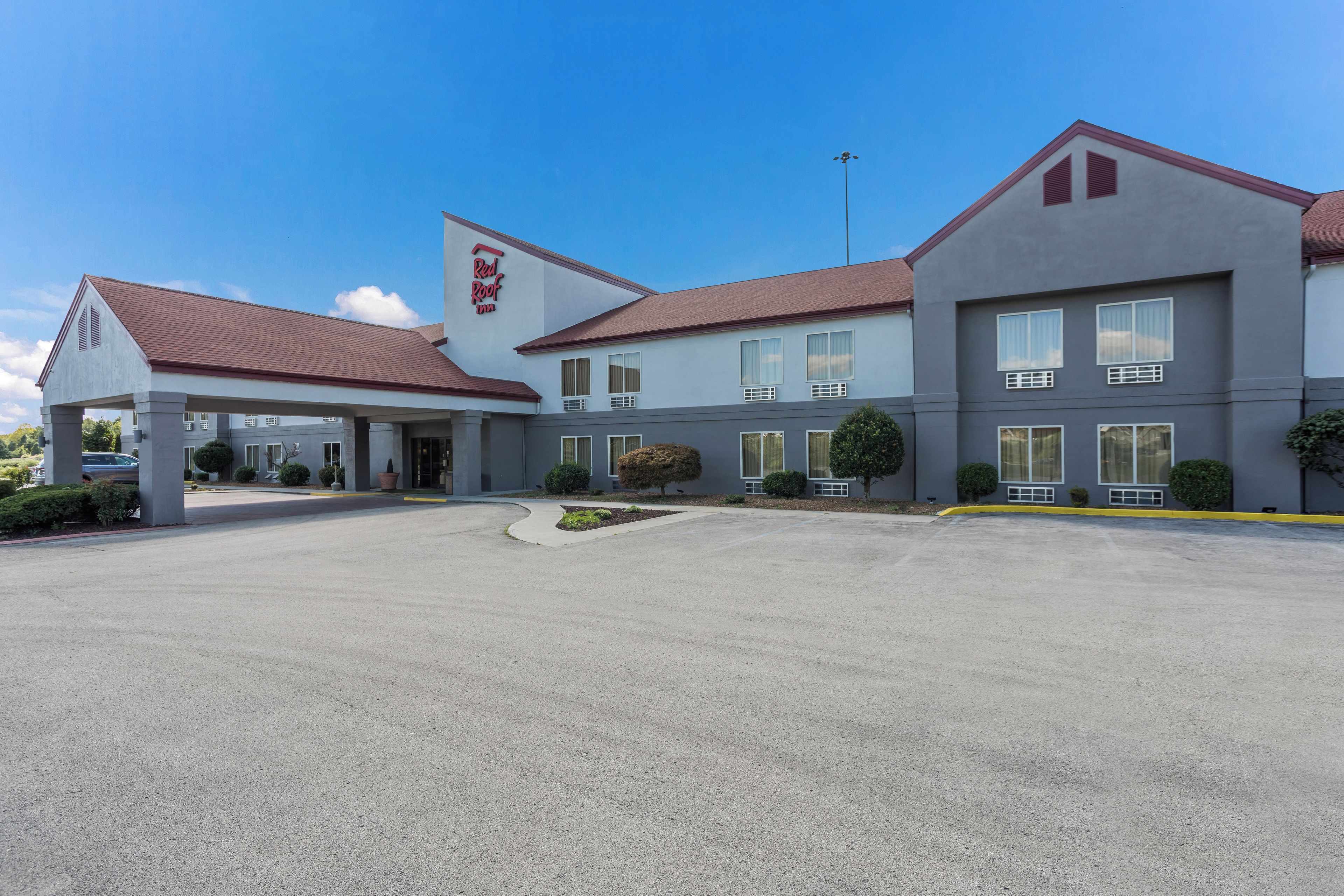 Ein Red Roof Inn mit überdachter Eingangspartie, Parkplatz und blauem Himmel.