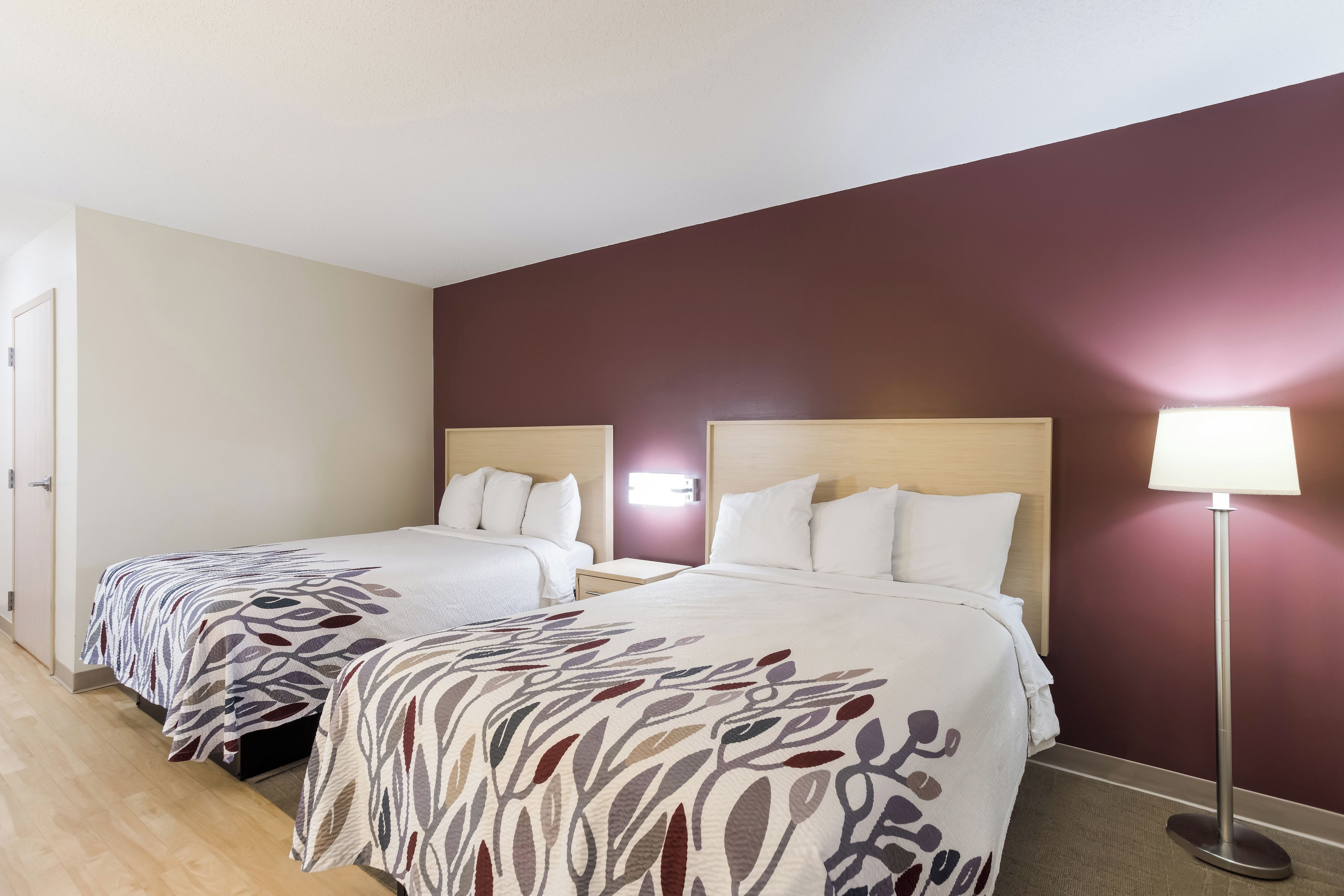 A hotel room with two beds, a nightstand, a lamp, and a door.
