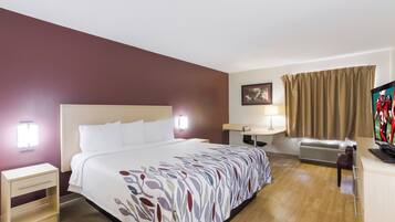 A hotel room with a bed, bedside table, lamp, TV, and an air conditioning unit.