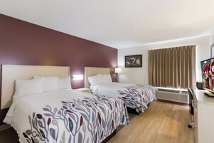 Una habitación de hotel con dos camas, un escritorio con computadora, una ventana con cortinas y un aire acondicionado de pared.