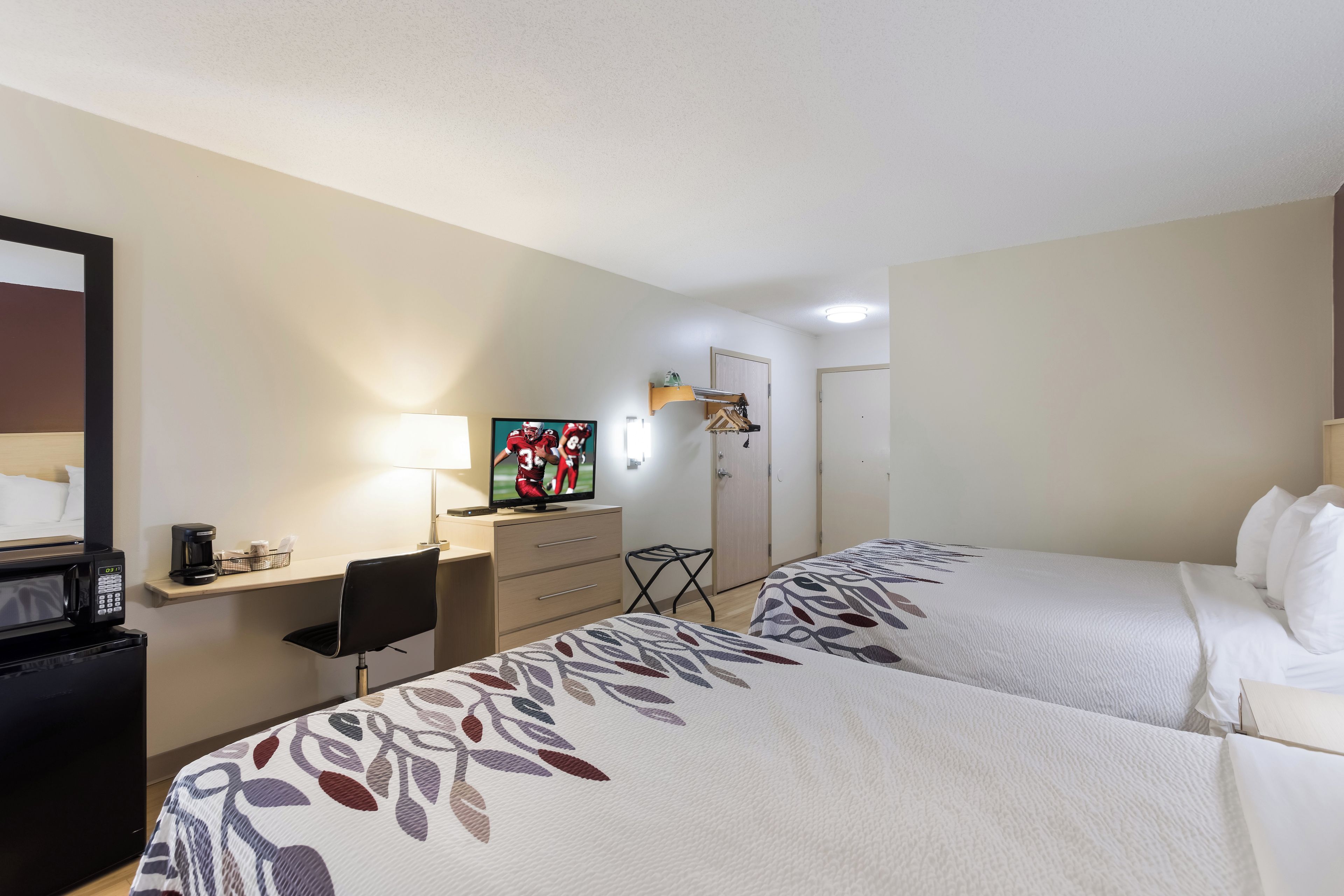 Habitación de hotel con dos camas, un escritorio con computadora, televisor y microondas.