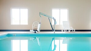 Une piscine avec un plongeoir et deux chaises blanches.