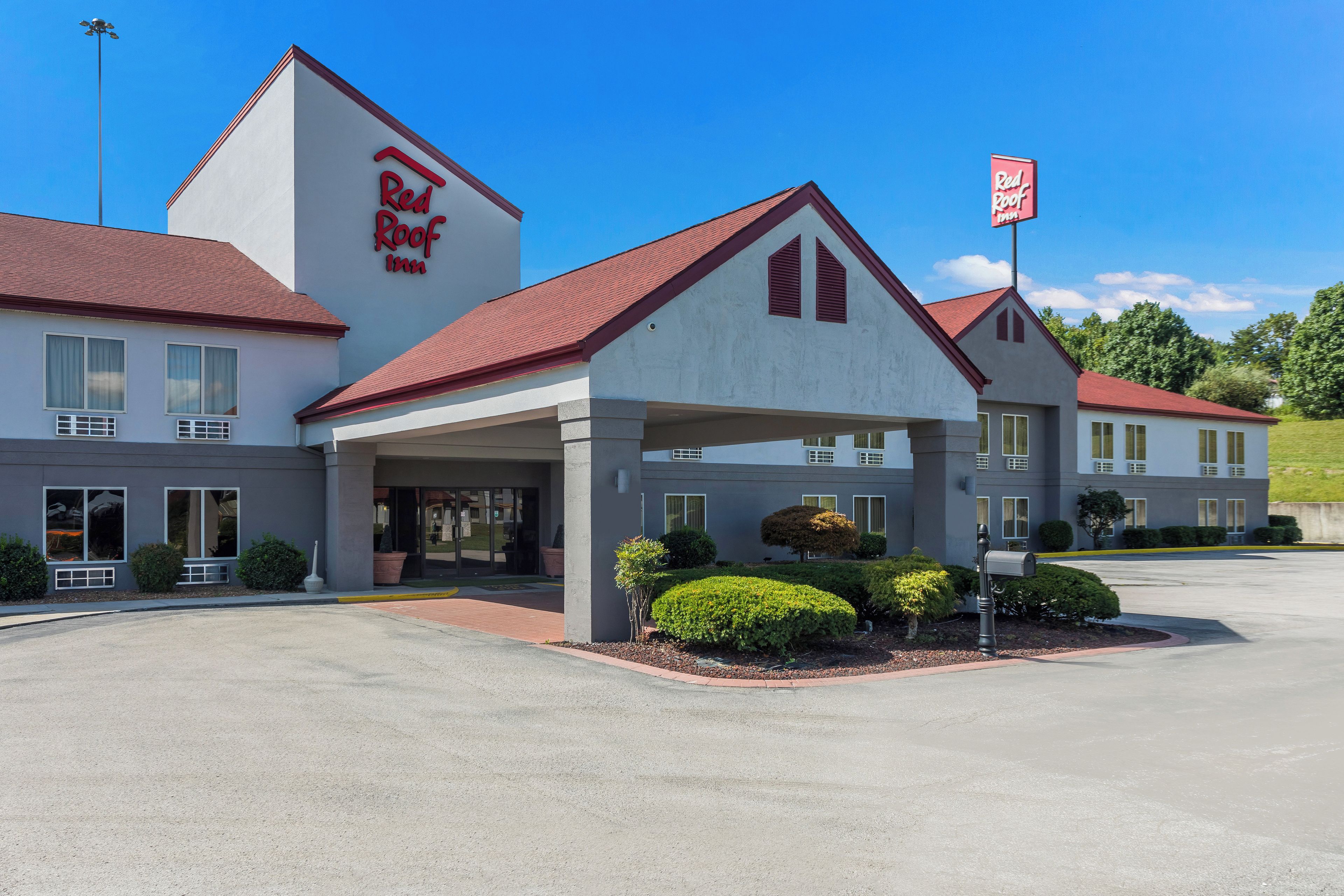 Red Roof Inn -hotelli, jossa on katettu sisäänkäynti, pysäköintialue ja kirkas taivas.